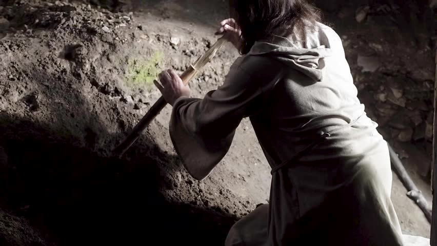 A man like Jesus Christ is digging a hole in the dungeon, a man is searching for a precious treasure, a man in a white robe is digging the earth with a stick and finds gold, Jesus hides the holy grail Royalty-Free Stock Footage #1018537753