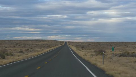 Drive Plate-Long straight road (SR 257) tapers to vanishing point in the far distance in the Great Basin Desert in Utah as sun lights dark clouds.