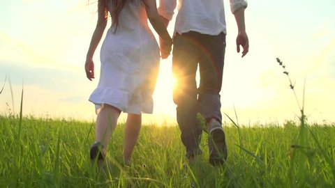Happy Young Couple Walking on Summer field and smiling, holding hands walk through a wide field, having fun outdoors. Countryside. Man and woman on the meadow. Sun flare. Slow motion Full HD 1080p