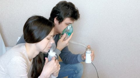 Use nebulizer and inhaler for the treatment. Man and woman inhaling through inhaler mask. Side view.