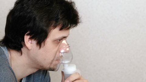 Use nebulizer and inhaler for the treatment. Young man inhaling through inhaler mask and coughs. Side view.