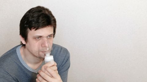 Use nebulizer and inhaler for the treatment. Young man inhaling through inhaler mask. Side view.