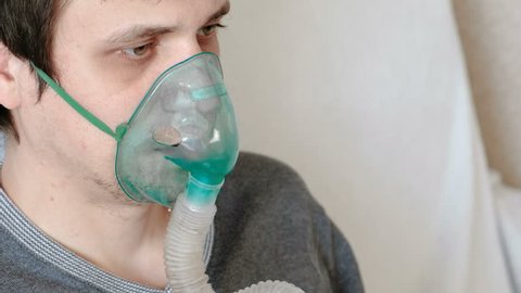 Use nebulizer and inhaler for the treatment. Closeup man's face inhaling through inhaler mask. Front view.