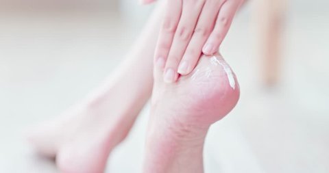 Woman sitting on bed and applying cream onto her foot at home