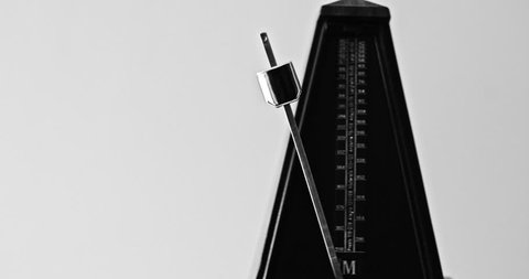 Black and white close-up shot of vintage metronome with pendulum beats slow rhythm on the gray background