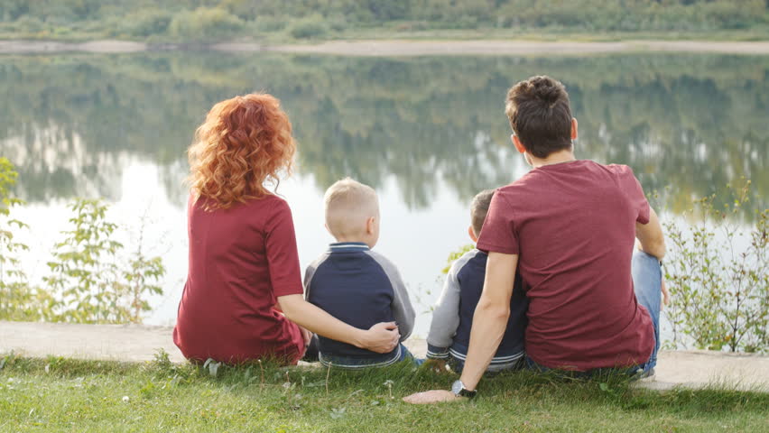 Family and children concept. Young couple with two sons walking by the river