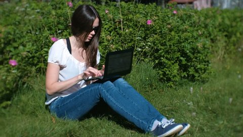 Beautiful brunette girl working typing on laptop sitting in Park in summer.