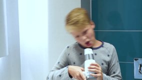 Portrait of cute handsome little kid dressed in pyjama singing and cheerfully dancing in bathroom. Boy uses hairdryer as microphone. Real time 4k video footage.
