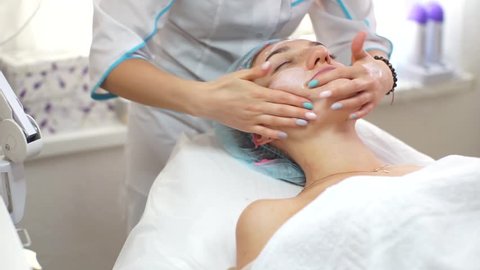 The beautician makes a girl a facial. Beautiful girl in a Spa salon. Woman lying at the reception at the beautician. The girl puts the cream on her face. Anti-aging facial massage.