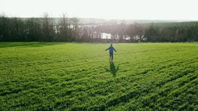 a little boy in a blue vest is running away to the river on the background of green field. Camera motion to right. Camera motion forward