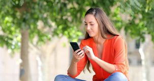 Excited woman using a smart phone finding good news sitting on a bench in a park