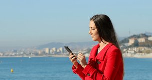 Side view portrait of a excited woman using a smart phone on the beach in winter