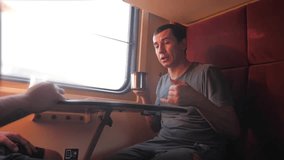 man is sitting on the train carriage holding a Railway and drinking coffee and tea. slow motion video. two men drinking tea on the train talking the train social media. man lifestyle with smartphones