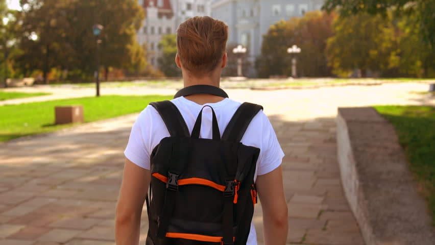 back view young man walking with backpack on the street. caucasian student with blond hair walks outdoor slow motion Royalty-Free Stock Footage #1018587700