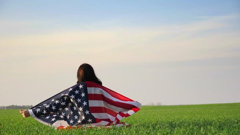 American woman sitting on green grass in a field wrapped a large United States flag