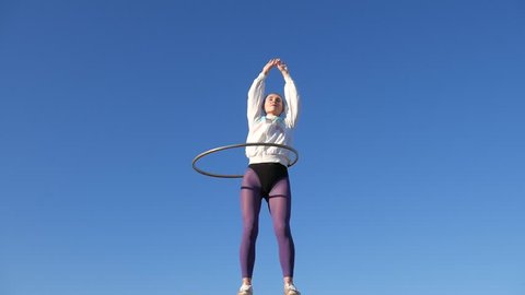 The girl turns the hoop, on the blue sky background. Clothing style 80 and 90's outfits.
