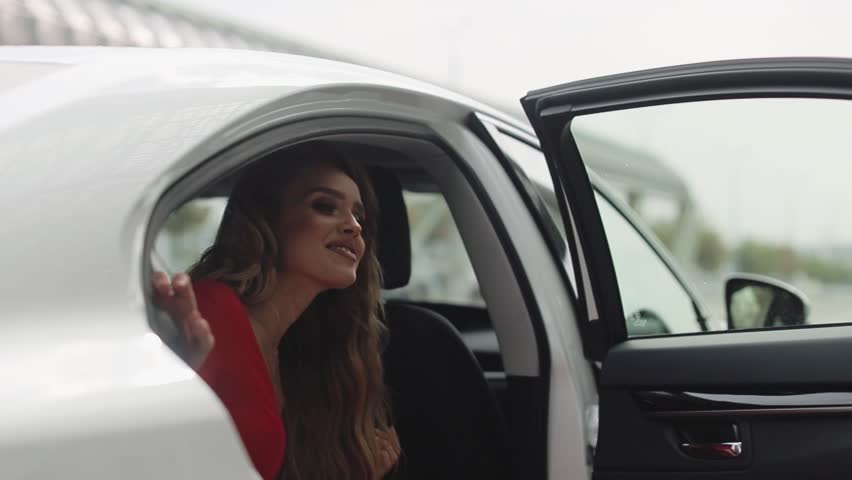 Fashion Model In Red Dress And High Heel Shoes Is Goes Out Of The White Car. Airport Terminal.