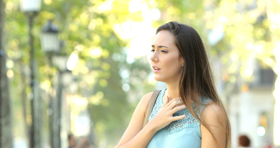 Asthmatic woman suffering an asthma attack and using inhaler in the street