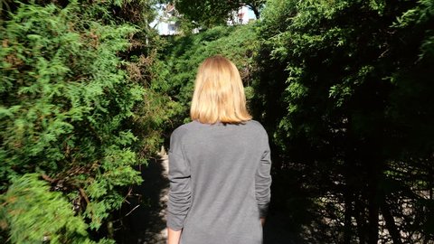 Enjoying Time Walking In Garden Maze. Tracking shot of a young woman walking through the bushes of a garden maze on a sunny day. Slow motion