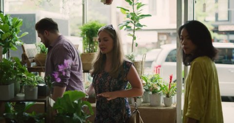 Worker helps young couple choose the perfect plant for their new home in interior boutique flower shop with soft day lighting. Medium shot on 4k RED camera.