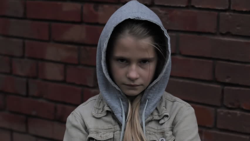 Dark portrait of sad displeased young girl looking at camera against brick wall. Difficult child wearing hooded jacket feeling of anger for having been offended standing alone outdoor. | Shutterstock HD Video #1018635619