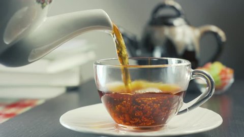 Tea being poured into glass transparent tea cup. Cup of tea.
Sweets, hot tea and teapot. Ceramic teapot and glass teacup closeup. Slow motion
