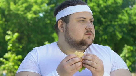 Fat man eating burger after workout, addicted to junk food, lack of willpower