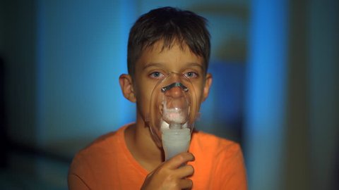 Teenage boy looks straight into the camera while breathes through nebulizer. asthma. inhaler. home medicine.