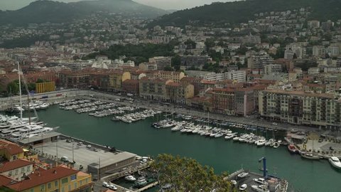 Locked down shot of port in French luxury resort Nice. Yachts and boats in the harbour. Cars are driving by. Locked down real time establishing shot