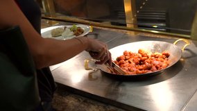This close up video shows a woman diner putting delicious fresh orange chicken on her plate at a buffet.
