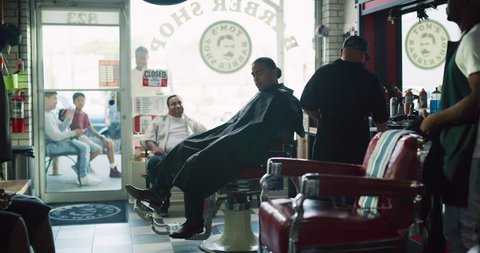 Happy cool male customers sitting in barber chair in interior hipster barbershop with soft day lighting. Wide shot on 4k RED camera on a gimbal. 