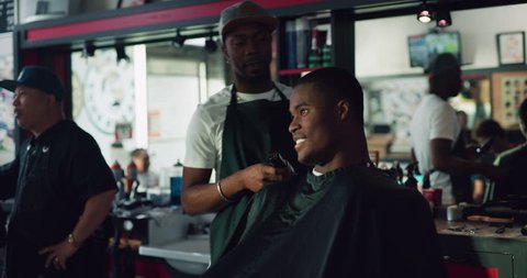 Young African American professional barber helping a customer in interior hipster barbershop with bright day lighting. Medium shot on 4k RED on a gimbal.