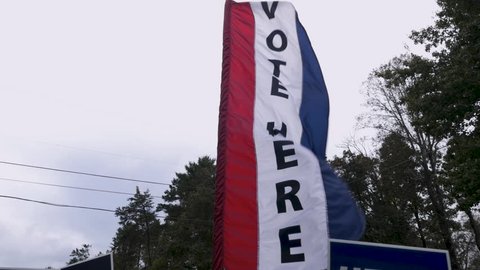 Slow motion of a red white and blue vote here sign blowing in the wind during an election
