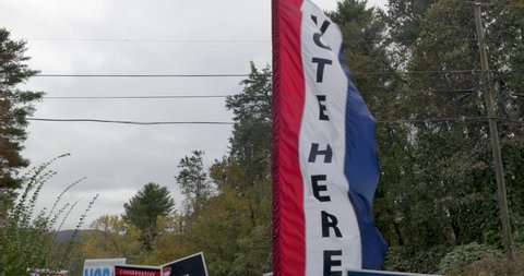 Red white and blue vote here sign blowing in the wind at the entrance to a voting location