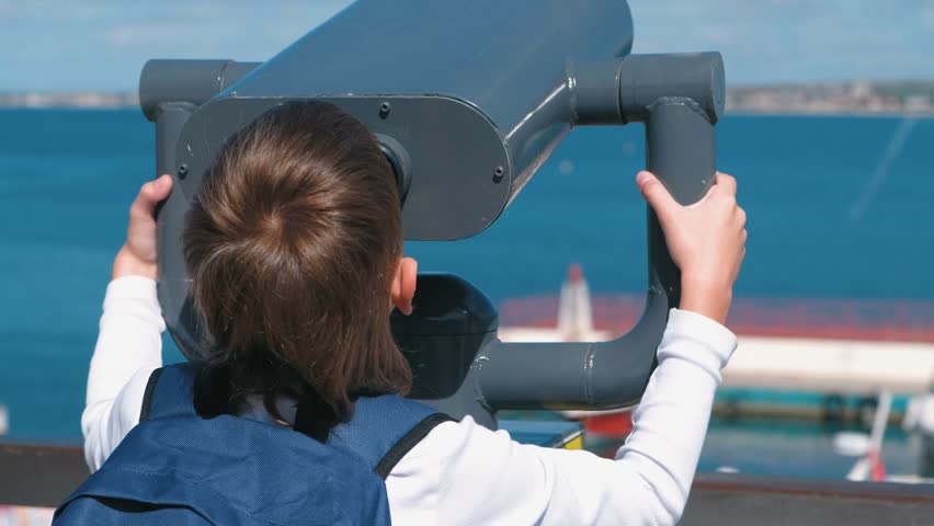 Unrecognizable boy looks through binoculars at the sea.