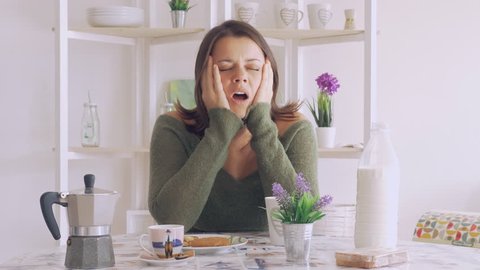 Cute young woman yawning during breakfast at home sleepy in the morning