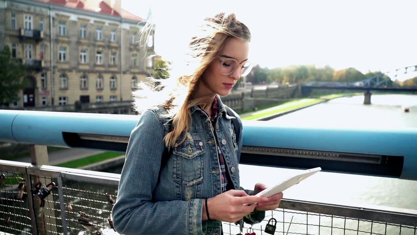 Young teen girl standing with tablet on the bridge in the city, super slow motion
