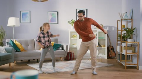 Happy Little Girl Dances with Young Father in the Middle of the Living Room. Happy Family Time, Father and Daughter Dancing at Home.