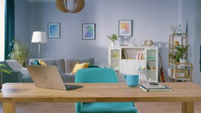Zoom In Shot of the Stylish Interior of the Living Room with Wooden Working Desk with Laptop, Stylish Chairs, Sofa. Tastefully Colorful Furniture with Serene Tones, Pleasant Art on the Walls.