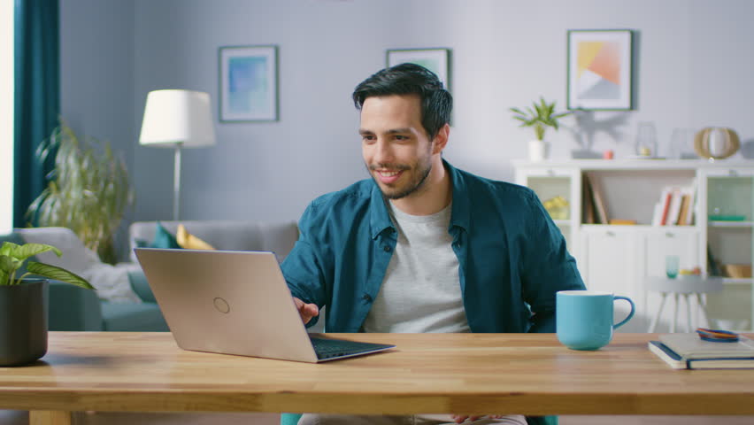 Happy Handsome Man Working on a Laptop Celebrates Successful Endeavor with YES Gesture. Freelances Working from His Living Room Has Stroke of Luck and Wins Big. Royalty-Free Stock Footage #1018666288