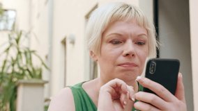 A pretty young blonde woman wearing a green dress sitting outside and using a phone. Close-up shot