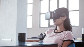 A beautiful young woman sitting in cafe making hand gestures wearing VR or Augmented reality glasses An attractive girl moving hands while exploring 3D visual space wearing visual reality goggles