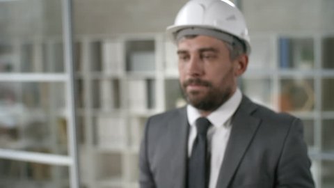 Medium shot of bearded man wearing suit and hard hat holding futuristic mobile phone. Footage suitable for adding AR graphics