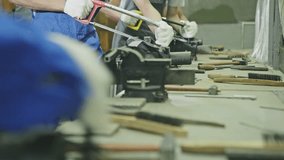 Row of workers working with hand saws over a workbench littered with tools in a factory production line in a close up low angle view