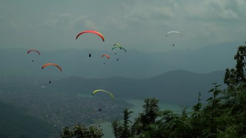 Paragligind in Népal - multiple paragliders in the sky above lake 