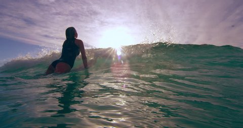 Athletic female surfer on surfboard swimming over a wave towards ocean in Australian beach with bright day lighting. Medium shot on 4k RED camera.