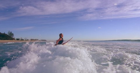 Athletic female surfer jumping on surfboard and swimming towards ocean in Australian beach with bright day lighting. Wide shot on 4k RED camera.
