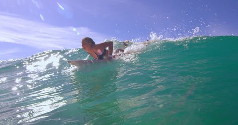 Eager blonde woman swimming with a large ocean wave on surfboard and having fun in Australian beach with bright day lighting. Wide shot on 4k RED camera.