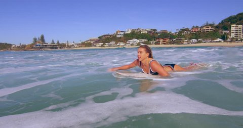 Happy female surfer swimming over calm ocean waves on surfboard in Australian beach with bright day lighting. Wide shot on 4k RED camera.