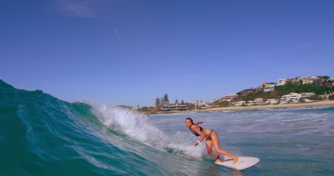 Skillful blonde woman surfing a large blue ocean wave and having fun in Australian beach with bright day lighting. Wide shot on 4k RED camera.